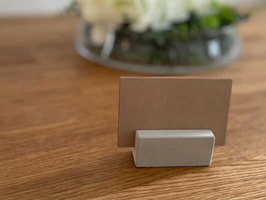 Kurzer Kartenhalter aus Beton mit Kraftpapier-Karte vor einem Blumengesteck
